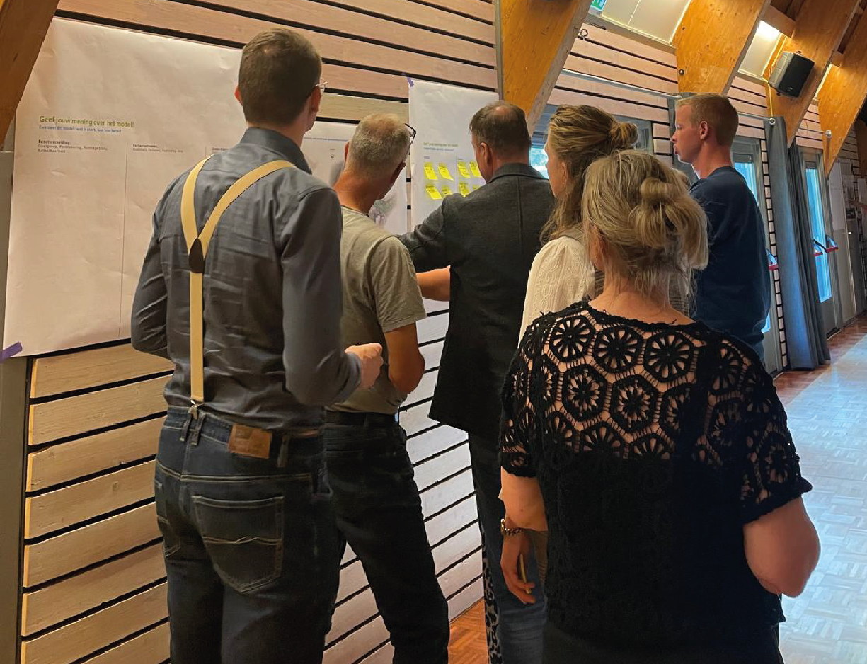 http://Mensen%20in%20een%20ruimte%20die%20om%20aandachtig%20naar%20een%20papier%20op%20de%20muur%20kijken%20en%20dit%20bespreken